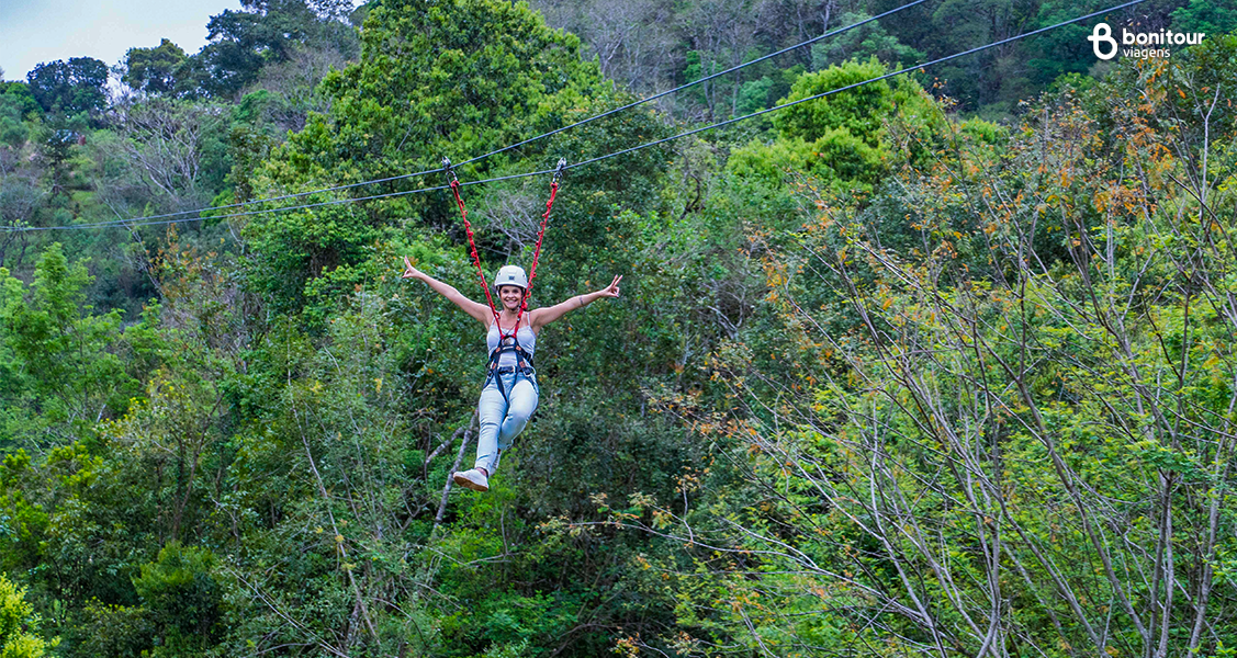 Viajante em passeio de tirolesa no Raft Adventure Park na Serra Gaúcha com árvores ao fundo
