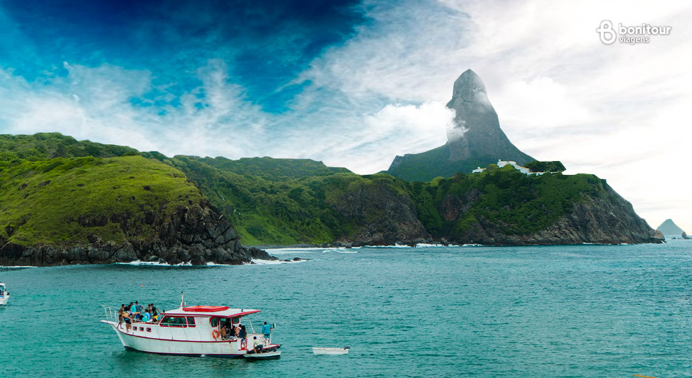 Imagem de barco nas águas de Fernando de Noronha com o morro do pico ao fundo